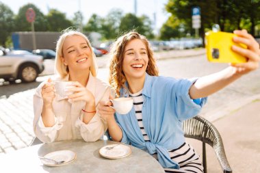 Kafede oturan mutlu güzel kızlar kamerayla selfie çeker. Moda, güzellik, blog, turizm.