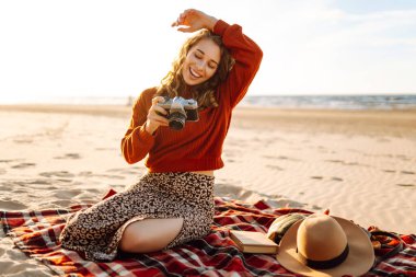 Sahilde retro kameralı mutlu bir kadın. Seyahat, hafta sonu, rahatlama ve yaşam tarzı konsepti.