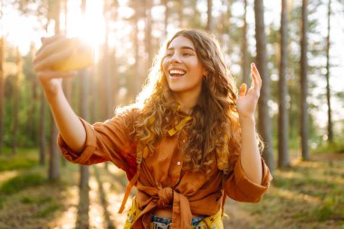 Güneşli bir ormanda yürürken fotoğrafını çeken güzel bir kadın. Doğadaki selfie. Macera, seyahat, tatil konsepti.