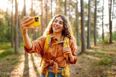 Güneşli bir ormanda yürürken fotoğrafını çeken güzel bir kadın. Doğadaki selfie. Macera, seyahat, tatil konsepti.