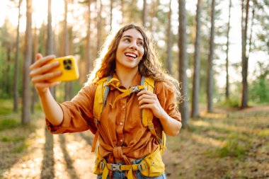 Güneşli bir ormanda yürürken fotoğrafını çeken güzel bir kadın. Doğadaki selfie. Macera, seyahat, tatil konsepti.