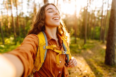 Güneşli bir ormanda yürürken fotoğrafını çeken güzel bir kadın. Doğadaki selfie. Macera, seyahat, tatil konsepti.
