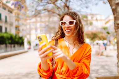 Cep telefonu kullanıp sokak pazarında rahatlayan genç ve mutlu bir bayan. Seyahat, turizm, teknoloji, blog, iletişim kavramı.