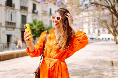 Cep telefonu kullanıp sokak pazarında rahatlayan genç ve mutlu bir bayan. Seyahat, turizm, teknoloji, blog, iletişim kavramı.