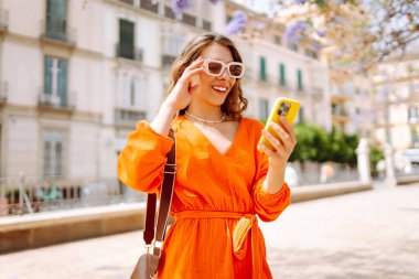 Cep telefonu kullanıp sokak pazarında rahatlayan genç ve mutlu bir bayan. Seyahat, turizm, teknoloji, blog, iletişim kavramı.