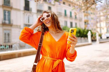 Cep telefonu kullanıp sokak pazarında rahatlayan genç ve mutlu bir bayan. Seyahat, turizm, teknoloji, blog, iletişim kavramı.