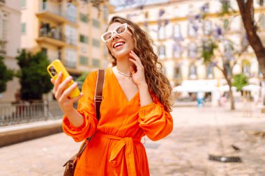 Cep telefonu kullanıp sokak pazarında rahatlayan genç ve mutlu bir bayan. Seyahat, turizm, teknoloji, blog, iletişim kavramı.