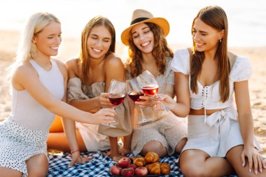Gülümseyen genç kadınlar kadeh tokuşturup birlikte vakit geçiriyorlar. Kumsalda kızlar partisi. Piknik, tatil, dinlenme, tatil.