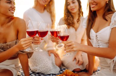 Gülümseyen genç kadınlar kadeh tokuşturup birlikte vakit geçiriyorlar. Kumsalda kızlar partisi. Piknik, tatil, dinlenme, tatil.