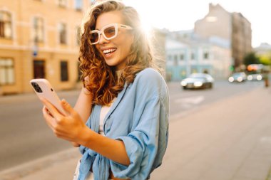 Şehirde telefonla dolaşan mutlu bir kadın portresi. Arkadaşlarla Online İletişim. Teknoloji, bağlantı, blog yazma, modern yaşam tarzı kavramı.