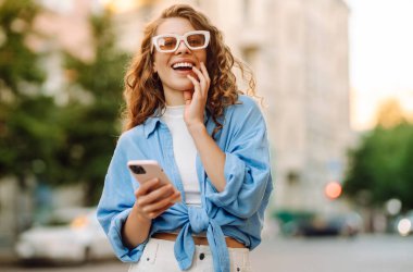 Şehirde telefonla dolaşan mutlu bir kadın portresi. Arkadaşlarla Online İletişim. Teknoloji, bağlantı, blog yazma, modern yaşam tarzı kavramı.