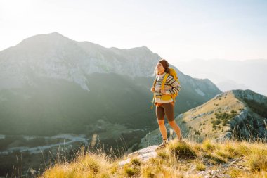 Kadın Gezgin, sırt çantasıyla dağlarda durup manzaraya hayran. Seyahat yaşam tarzı. Açık havada yaz tatili kavramları.