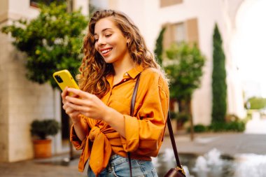 Şehirde kaldırımda yürürken akıllı bir telefon kullanan genç bir kadın. İş, teknoloji, blog, iletişim kavramı.