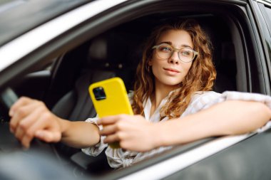 Kadın sürücü arabada akıllı telefon kullanıyor. Boş zaman, seyahat, teknoloji, navigasyon.