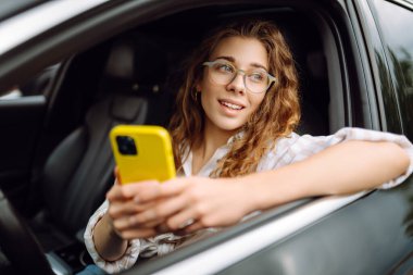 Kadın sürücü arabada akıllı telefon kullanıyor. Boş zaman, seyahat, teknoloji, navigasyon.