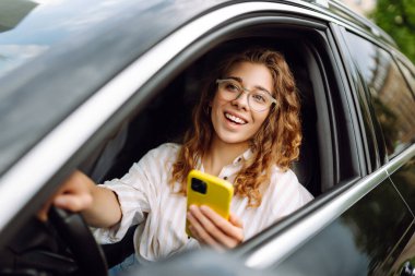 Kadın sürücü arabada akıllı telefon kullanıyor. Boş zaman, seyahat, teknoloji, navigasyon.