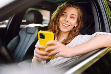 Kadın sürücü arabada akıllı telefon kullanıyor. Boş zaman, seyahat, teknoloji, navigasyon.