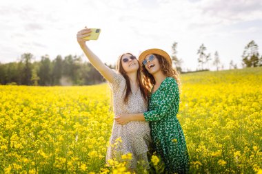 Çiçek tarlasında akıllı telefondan selfie çeken arkadaşlar. Moda, güzellik konsepti. Yaz manzarası.