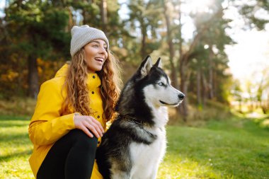 Genç bir kadın, parktaki çimenlikte köpeğiyle yürüyor. Birlikte oynuyoruz. Arkadaşlık kavramı, evcil hayvan, tatil.