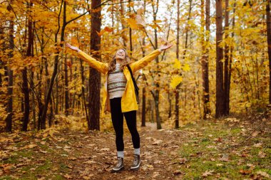 Gülümseyen genç kadın ormanda sonbahar havasının tadını çıkarıyor. Sonbahar manzarası.