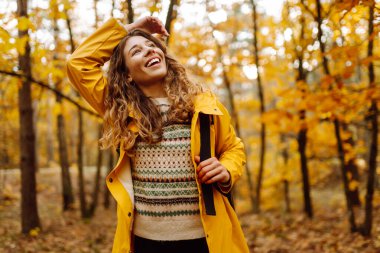 Gülümseyen genç kadın ormanda sonbahar havasının tadını çıkarıyor. Sonbahar manzarası.