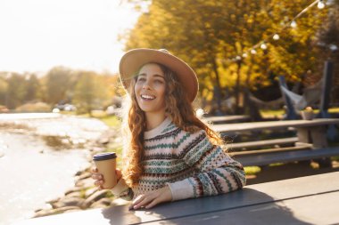 Genç bir kadın gölün arka planında kahve içerek rahatlıyor. Seyahat, kamp, doğa konsepti.