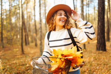Sonbahar manzarasında şehir ormanında bisiklet süren mutlu bir kadın. Aktif turist güneşli havanın tadını çıkarıyor. Hafta sonu konsepti.
