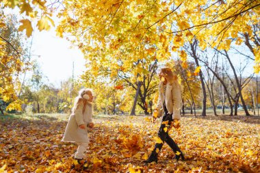 Aile günü. Genç anne ve küçük kızı sonbahar parkında eğleniyor ve dinleniyor. Çocuğa annelik ve sevgi.