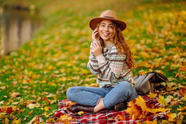 Süveter ve şapka içinde şık bir kadın portresi sonbahar doğasını seviyor. İnsanlar, özgürlük, yaşam tarzı, seyahat ve tatil kavramı.