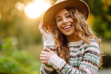 Süveter ve şapka içinde şık bir kadın portresi sonbahar doğasını seviyor. İnsanlar, özgürlük, yaşam tarzı, seyahat ve tatil kavramı.