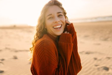 Gün batımında sahilde güzel bir kadının portresi. Kız plaj boyunca yürüyor ve sıcak sonbahar havasının tadını çıkarıyor. Seyahat, hafta sonu, rahatlama ve yaşam tarzı konsepti.