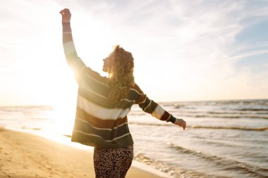 Gün batımında sahilde güzel bir kadının portresi. Kız plaj boyunca yürüyor ve sıcak sonbahar havasının tadını çıkarıyor. Seyahat, hafta sonu, rahatlama ve yaşam tarzı konsepti.