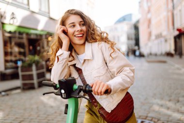 Elektrikli scooter kullanan güzel bir genç kadın. Sokak tarzı, ekolojik ulaşım. Etkin yaşam biçimi.