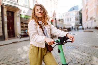 Elektrikli scooter kullanan güzel bir genç kadın. Sokak tarzı, ekolojik ulaşım. Etkin yaşam biçimi.