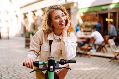 Elektrikli scooter kullanan güzel bir genç kadın. Sokak tarzı, ekolojik ulaşım. Etkin yaşam biçimi.