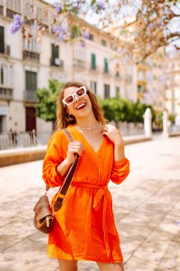 Güneşli bir günde sokakta poz veren gülümseyen bir manken. Açık havada şık bir bayan. Yaşam tarzı, tatil, tarz, seyahat kavramı.