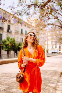 Güneşli bir günde sokakta poz veren gülümseyen bir manken. Açık havada şık bir bayan. Yaşam tarzı, tatil, tarz, seyahat kavramı.