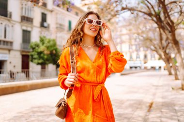Güneşli bir günde sokakta poz veren gülümseyen bir manken. Açık havada şık bir bayan. Yaşam tarzı, tatil, tarz, seyahat kavramı.