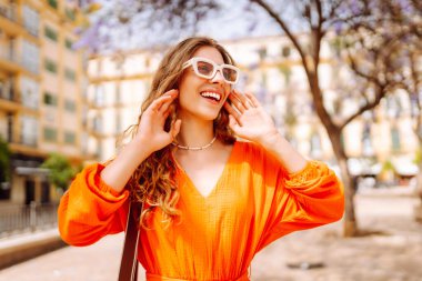 Güneşli bir günde sokakta poz veren gülümseyen bir manken. Açık havada şık bir bayan. Yaşam tarzı, tatil, tarz, seyahat kavramı.