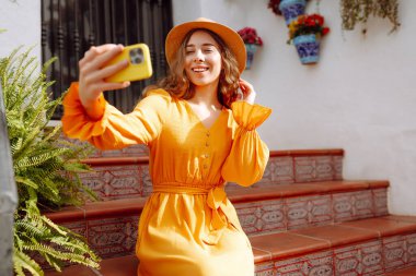 Sokakta selfie çekerken akıllı telefon kamerasına poz veren ve gülümseyen güzel bir genç kadın. Seyahat, blog, hafta sonu, rahatlama ve yaşam tarzı konsepti.