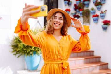 Sokakta selfie çekerken akıllı telefon kamerasına poz veren ve gülümseyen güzel bir genç kadın. Seyahat, blog, hafta sonu, rahatlama ve yaşam tarzı konsepti.