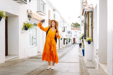 Sokakta selfie çekerken akıllı telefon kamerasına poz veren ve gülümseyen güzel bir genç kadın. Seyahat, blog, hafta sonu, rahatlama ve yaşam tarzı konsepti.