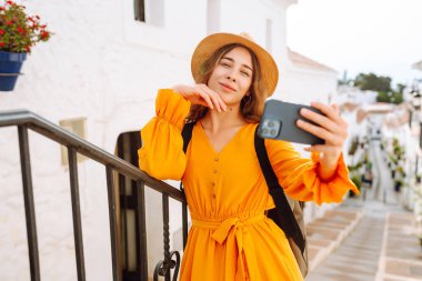 Sokakta selfie çekerken akıllı telefon kamerasına poz veren ve gülümseyen güzel bir genç kadın. Seyahat, blog, hafta sonu, rahatlama ve yaşam tarzı konsepti.