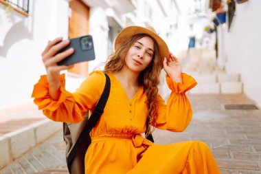 Sokakta selfie çekerken akıllı telefon kamerasına poz veren ve gülümseyen güzel bir genç kadın. Seyahat, blog, hafta sonu, rahatlama ve yaşam tarzı konsepti.