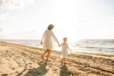 Anne gün batımında tatil sırasında kızıyla sahilde yürür. Seyahat, turizm, hafta sonu konsepti. Aile partisi.