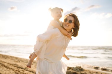 Anne gün batımında tatil sırasında kızıyla sahilde yürür. Seyahat, turizm, hafta sonu konsepti. Aile partisi.