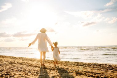 Anne gün batımında tatil sırasında kızıyla sahilde yürür. Seyahat, turizm, hafta sonu konsepti. Aile partisi.