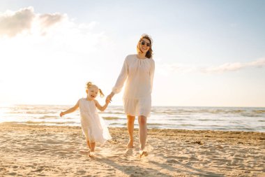 Anne gün batımında tatil sırasında kızıyla sahilde yürür. Seyahat, turizm, hafta sonu konsepti. Aile partisi.