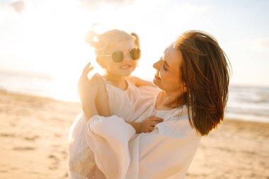 Anne gün batımında tatil sırasında kızıyla sahilde yürür. Seyahat, turizm, hafta sonu konsepti. Aile partisi.