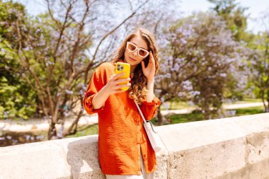 Genç bir kadın akıllı telefon kullanıyor ve şehirde yürürken gülümsüyor. İş, teknoloji, blog, iletişim kavramı.